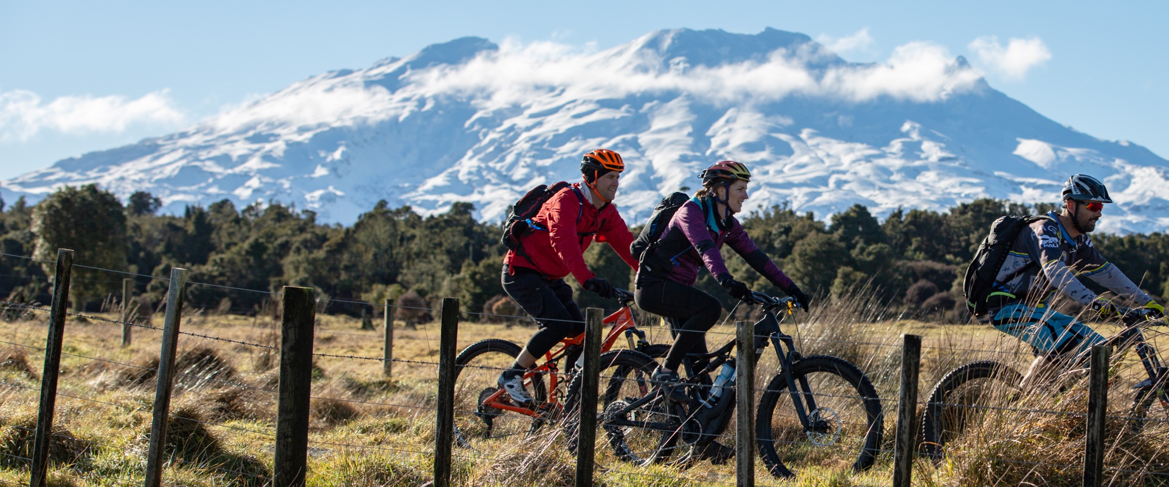 People on mountain bikes on Ohakune Old Coach Road with Mt Ruapehu covered in snow in the background.